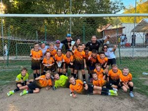 Équipe en maillot orange posant avec ses éducateurs devant le but