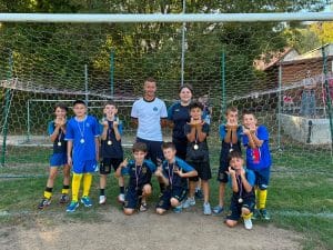 Équipe en maillot bleu clair posant avec son éducatrice devant le but
